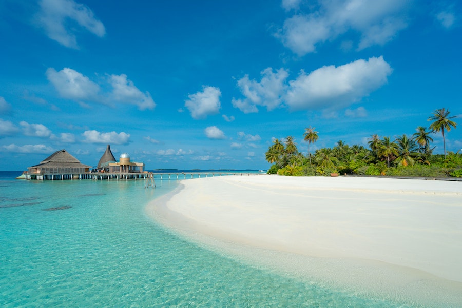 Plage de sable blanc des Maldives avec villas sur pilotis en fond